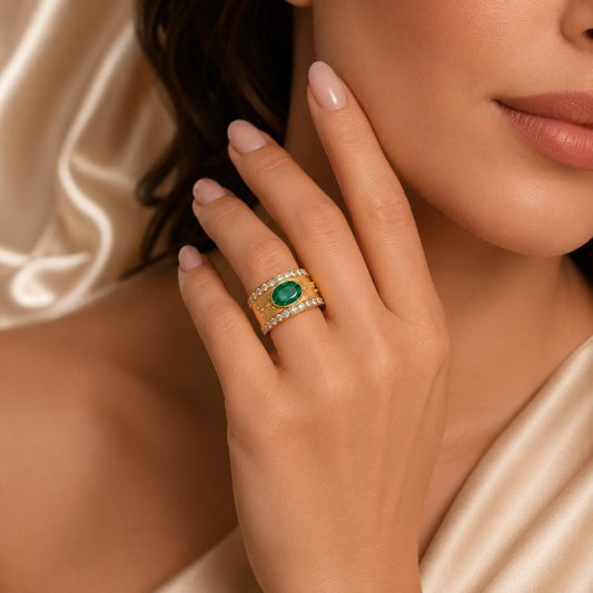 A close-up of a woman's hand wearing a gold ring with a large green gemstone, resting on her finger.