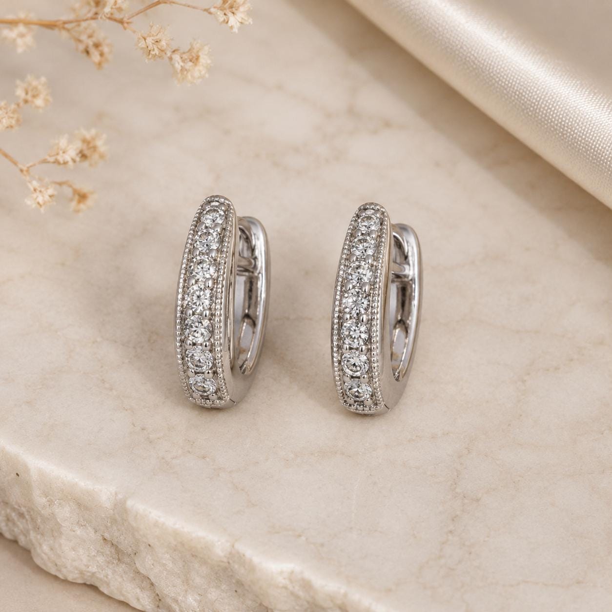 A pair of elegant silver earrings with a row of small diamonds set in the center, resting on a marble surface.
