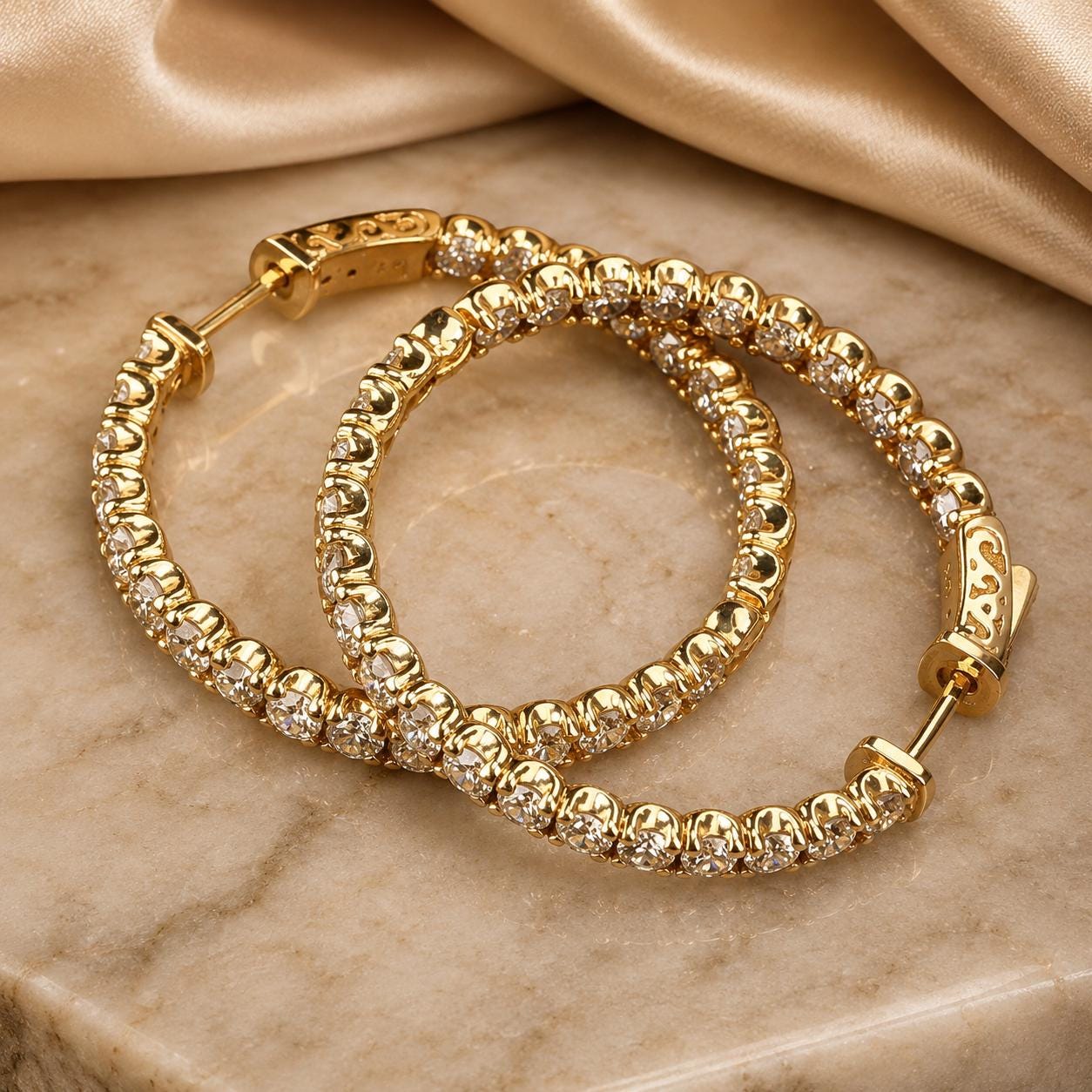 A pair of gold hoop earrings with small diamonds set in a beige fabric background.