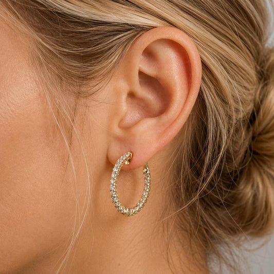 A close-up of a person's ear wearing a gold hoop earring with a sparkling crystal design.