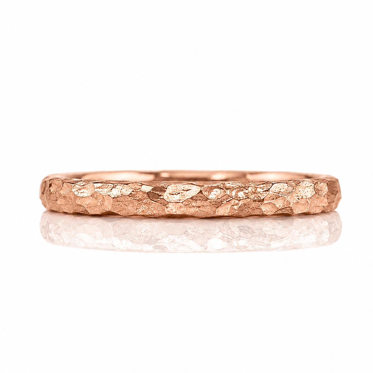 A close-up image of a rose gold ring with a textured surface, reflecting on a white background.