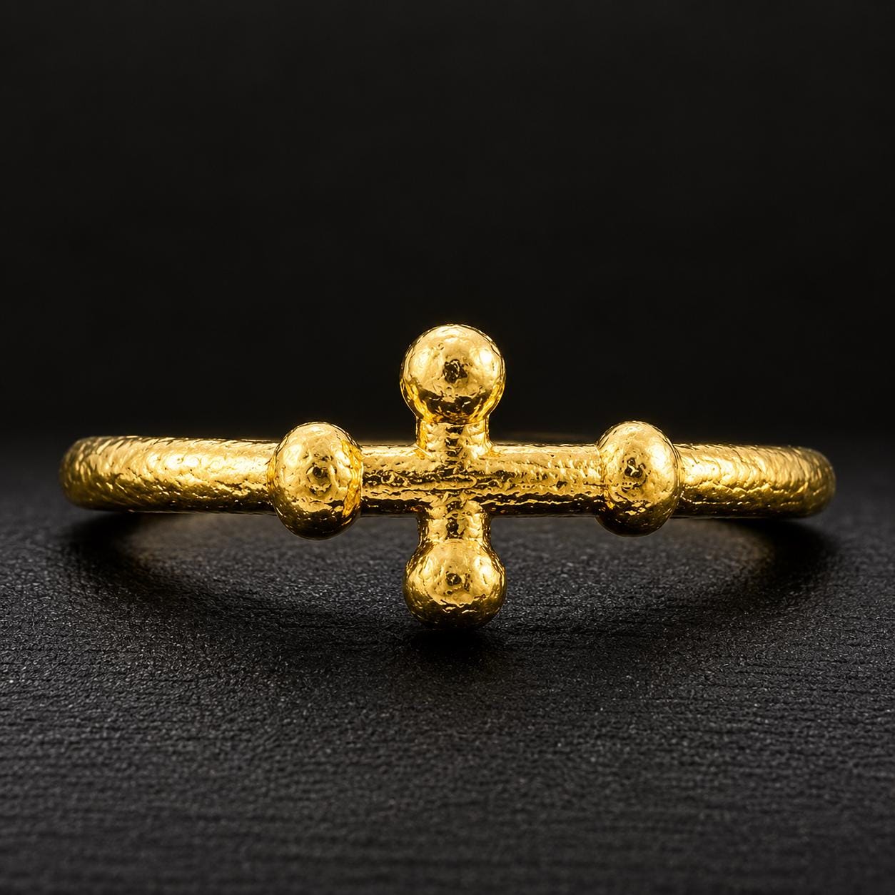 A gold bracelet with a unique design, featuring three small balls arranged in a cross shape on a black background.