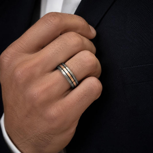 A close-up of a man's hand wearing a ring on the ring finger, with a black jacket visible in the background.