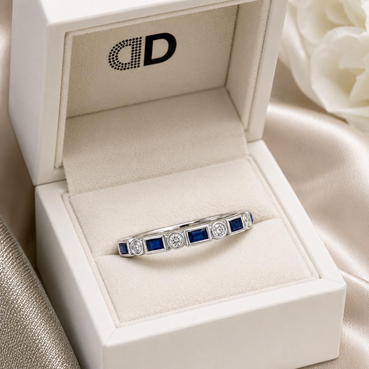 A white jewelry box containing a silver ring with blue gemstones.