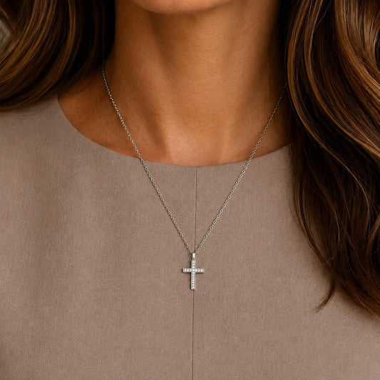 A close-up view of a woman's neck and chest area, showing a silver cross pendant necklace with a diamond accent.