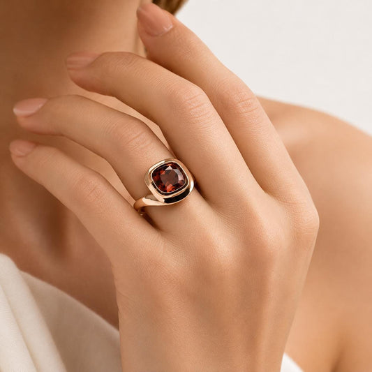 A close-up of a person's hand wearing a gold ring with a large, deep red gemstone.