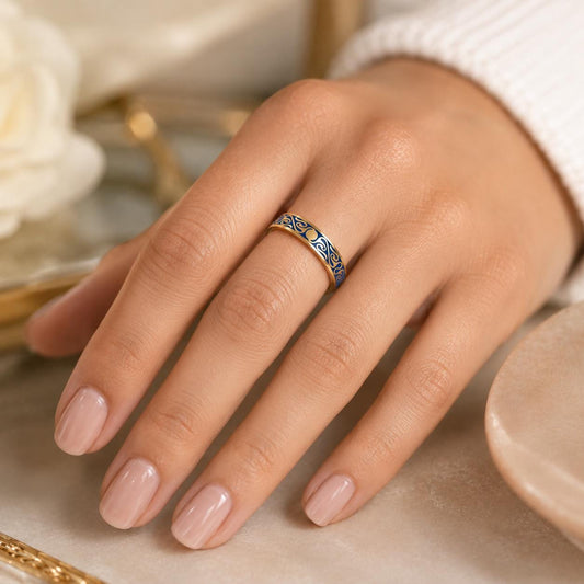 A close-up of a hand wearing a gold ring with blue and gold designs.
