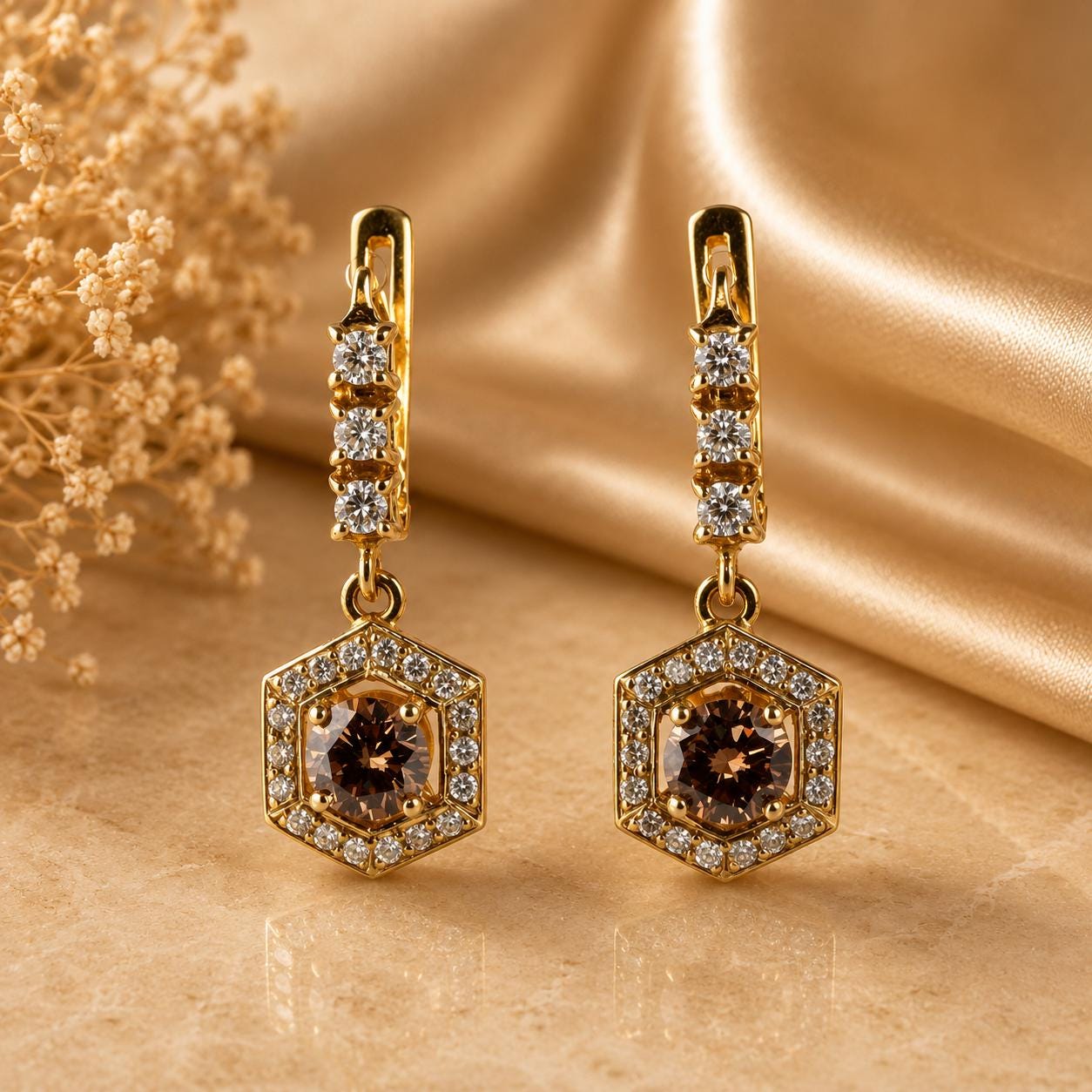 A pair of elegant gold earrings with a hexagonal center and sparkling diamonds, resting on a golden fabric background.