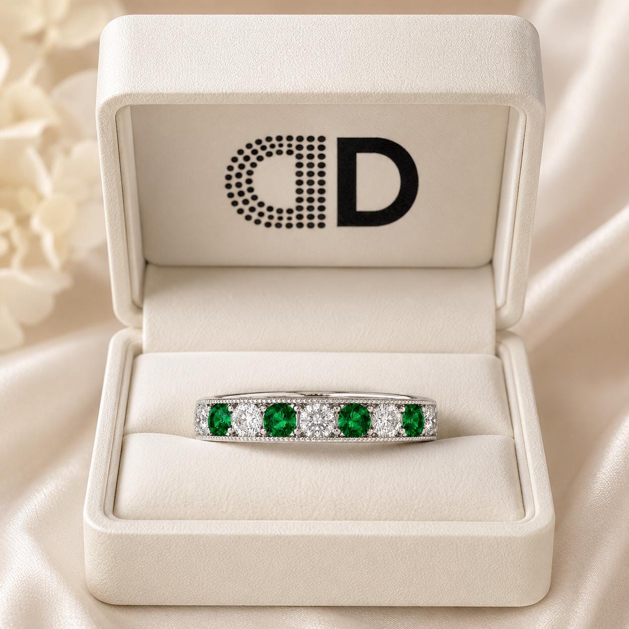 A white jewelry box containing a ring with a band of green and white diamonds, and a logo on the front of the box.