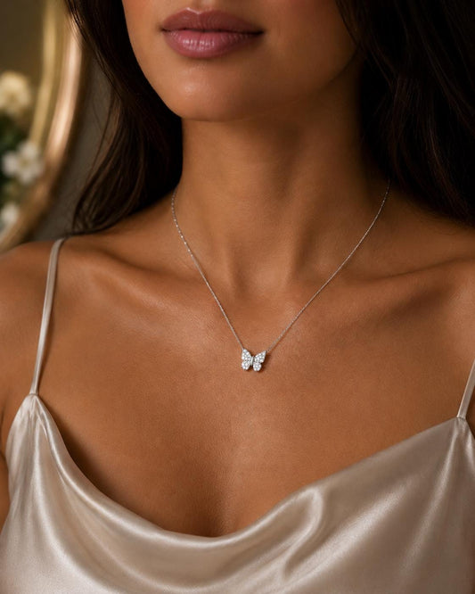 A close-up of a woman wearing a delicate silver necklace with a small butterfly pendant.
