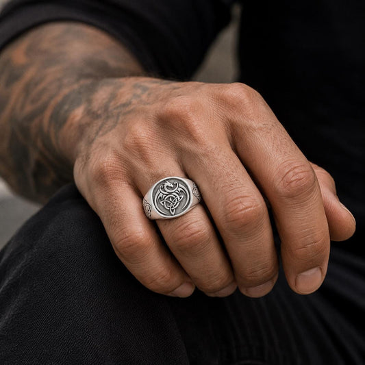 A close-up of a person's hand wearing a silver ring with a dragon design.