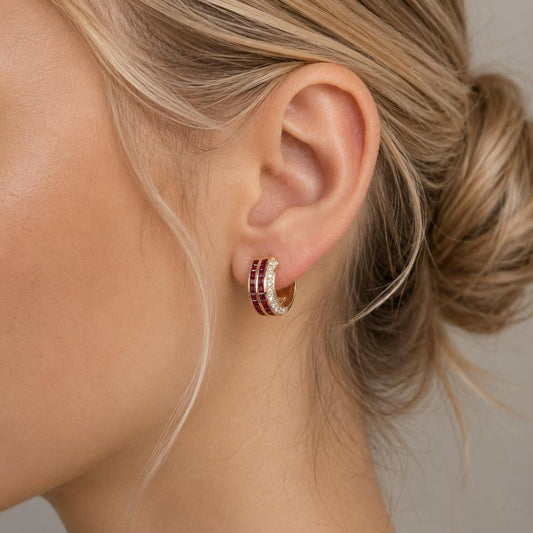 A close-up of a woman's ear adorned with a gold hoop earring featuring a stack of three red gemstones.