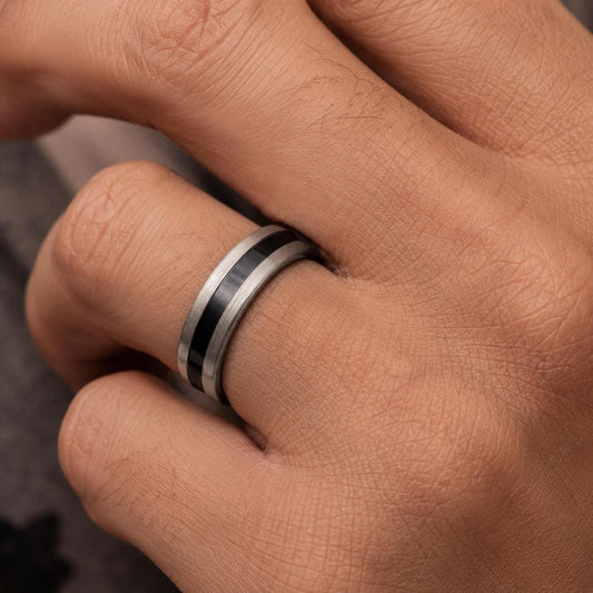 A close-up view of a person's hand wearing a silver ring with a black band.