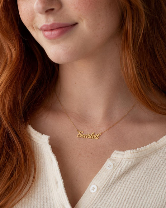 A close-up of a woman's neck and chest area, with a gold necklace featuring the name "Scrooge" on it.