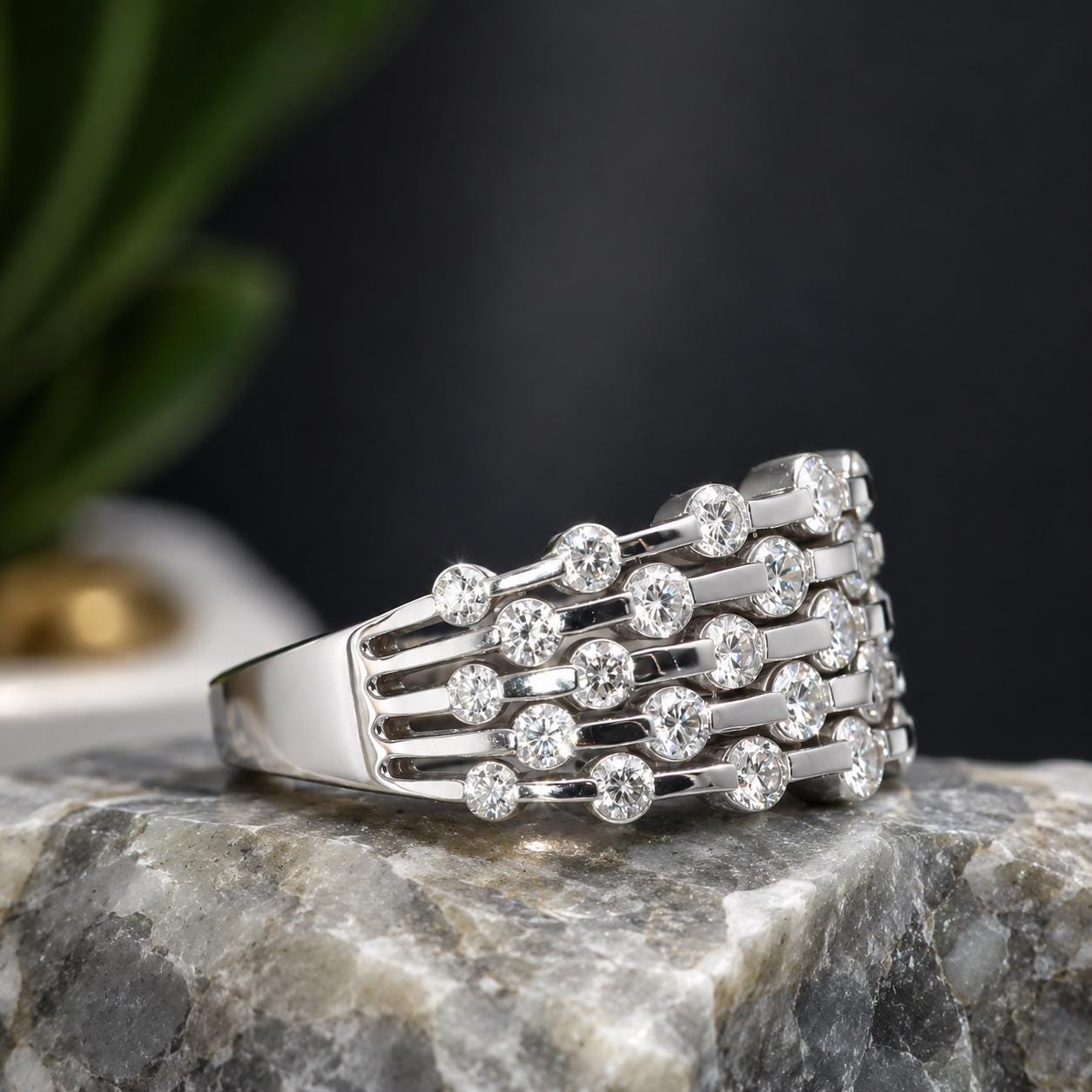 A silver ring with numerous small diamonds set in a unique design, resting on a gray rock.