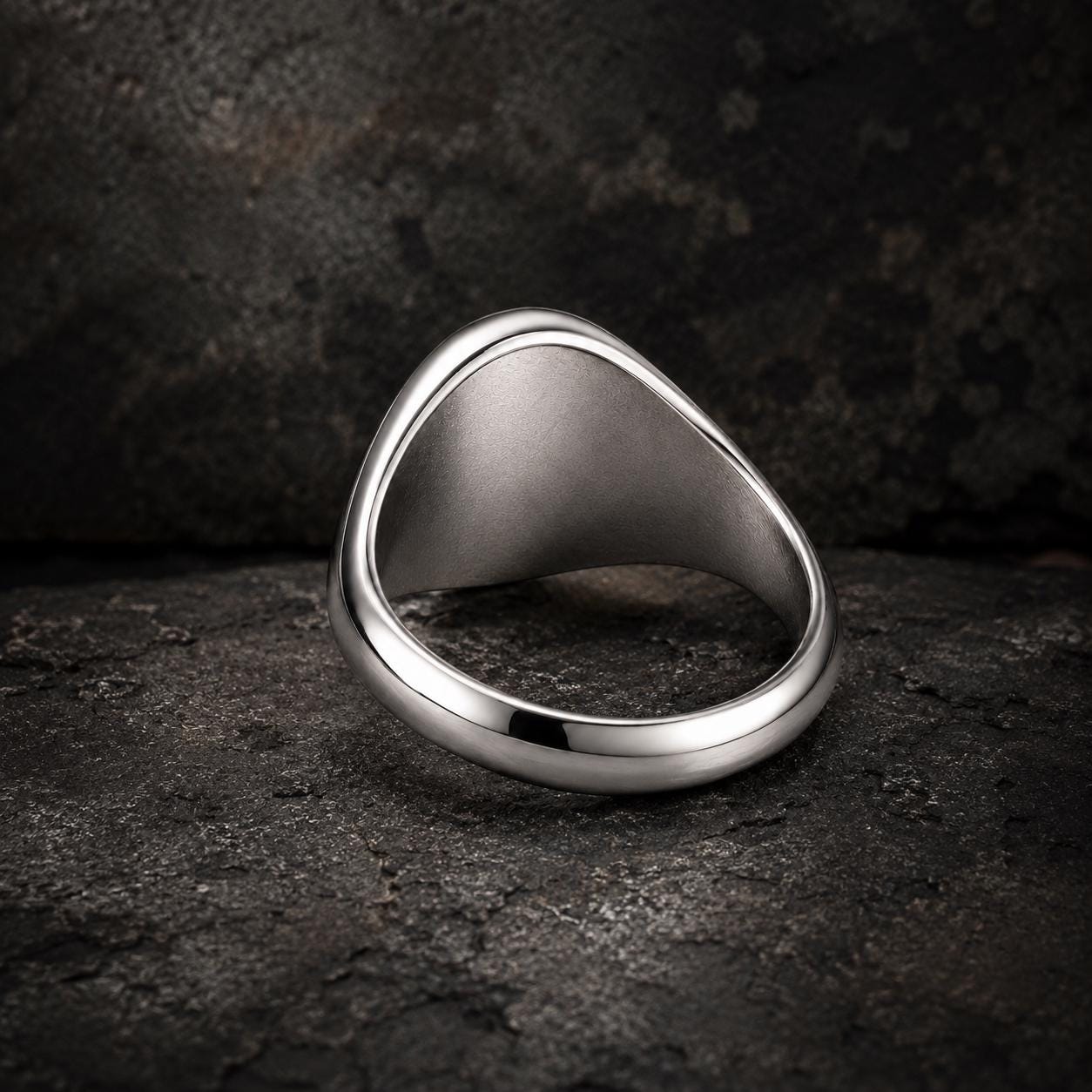 A silver ring with a unique, curved design sits on a dark, textured surface.