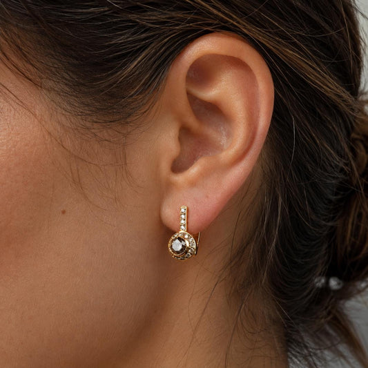 A close-up view of a person's ear adorned with a gold earring featuring a small gemstone.