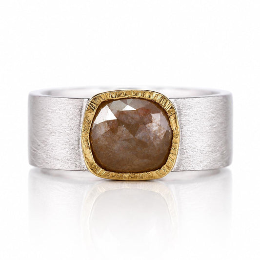 A silver ring with a large, irregularly shaped diamond set in a gold-colored band.