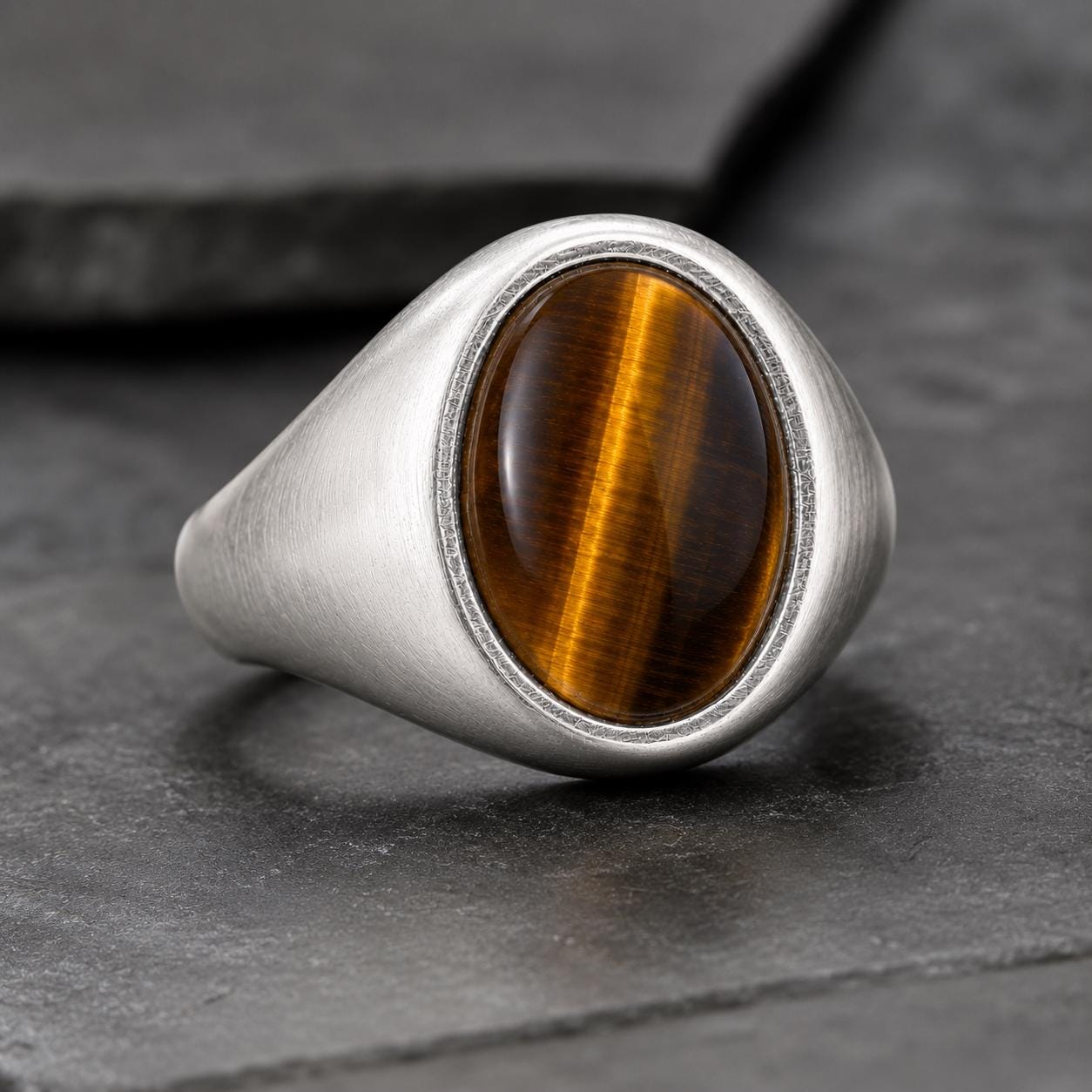 A silver ring with a large oval-shaped gemstone, likely a tiger eye, set in the center of the ring.