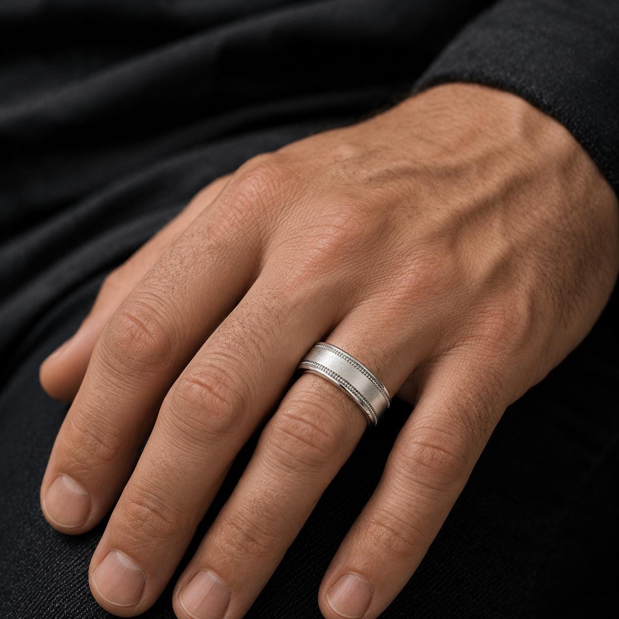 A close-up of a person's hand wearing a silver ring on the ring finger.