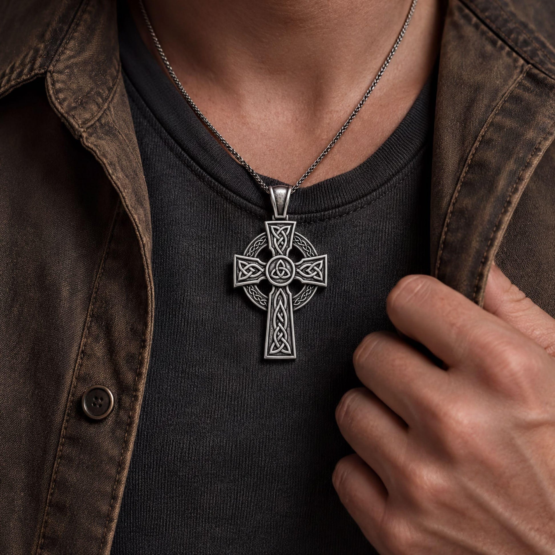 A silver cross pendant necklace is worn around a person's neck, with their hand visible on the right side of the frame.