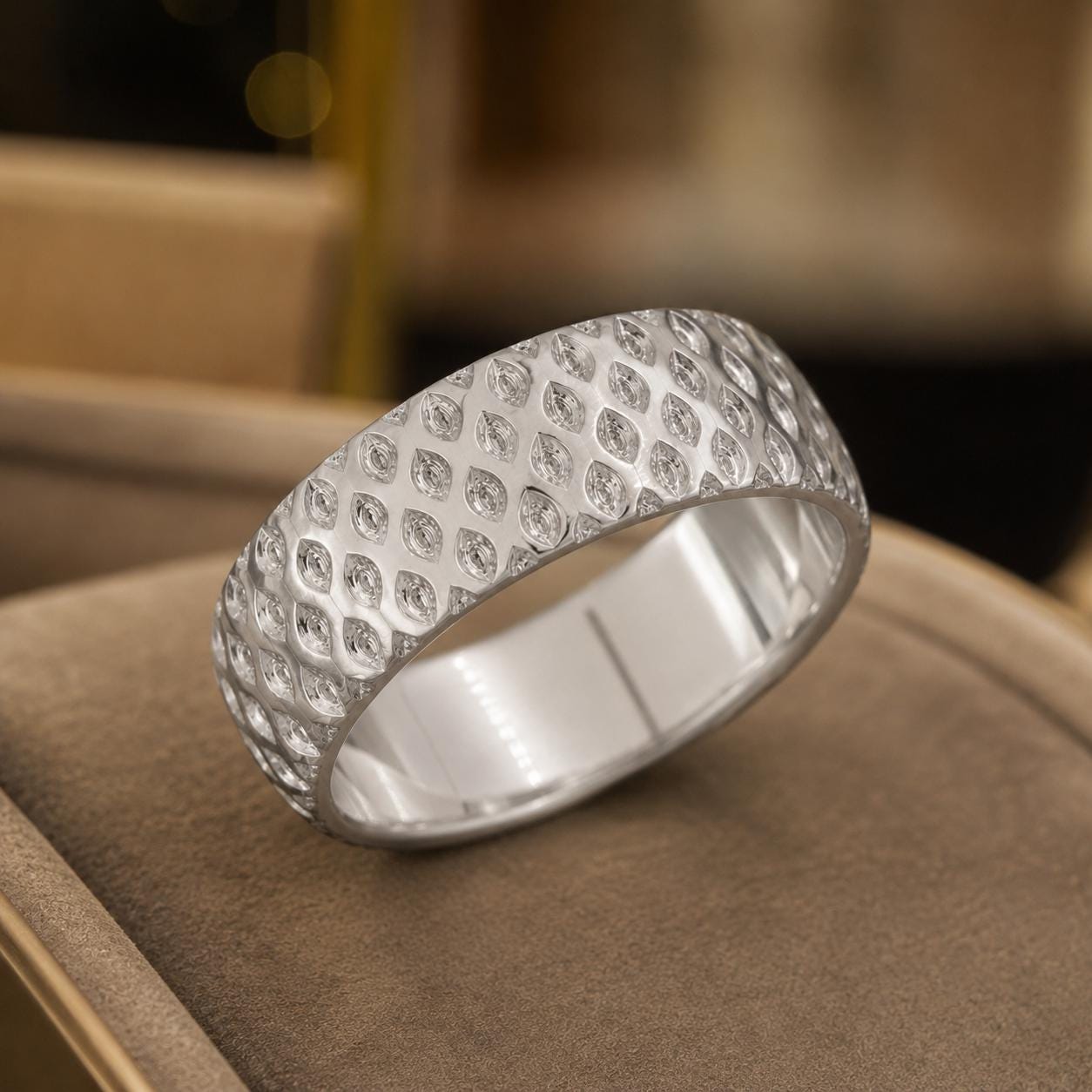 A silver ring with a diamond pattern sits on a brown surface.