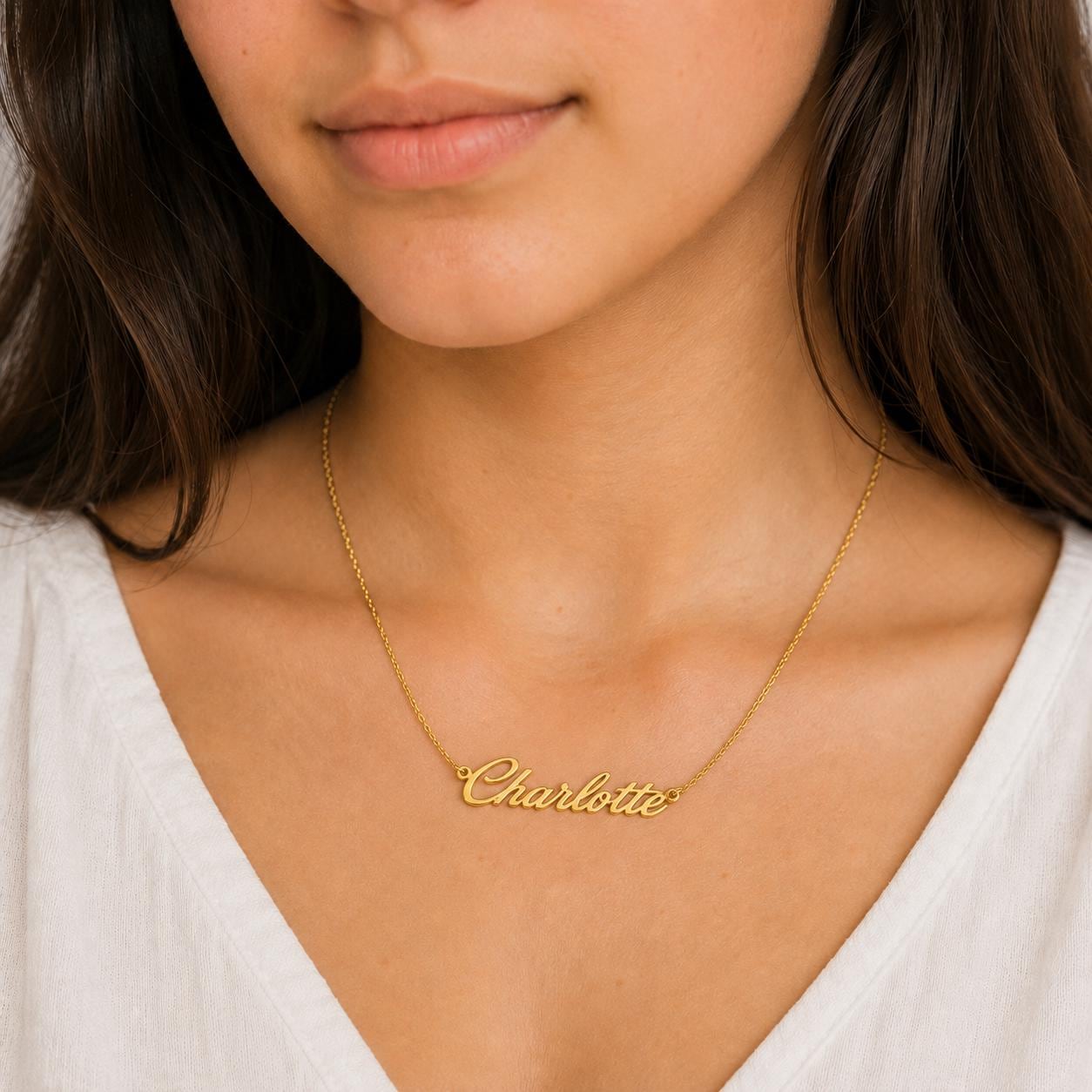 A close-up of a woman's neck and chest area wearing a gold necklace with the name "Charlotte" engraved on it.