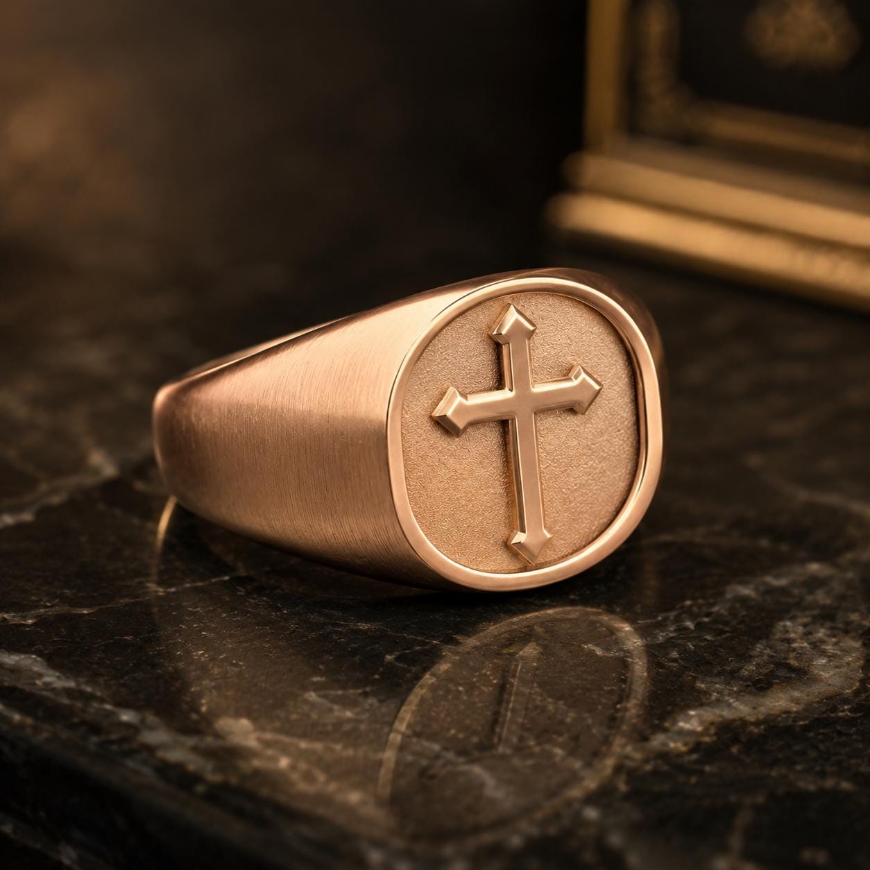 A gold-colored signet ring with a cross symbol on it, resting on a dark surface.