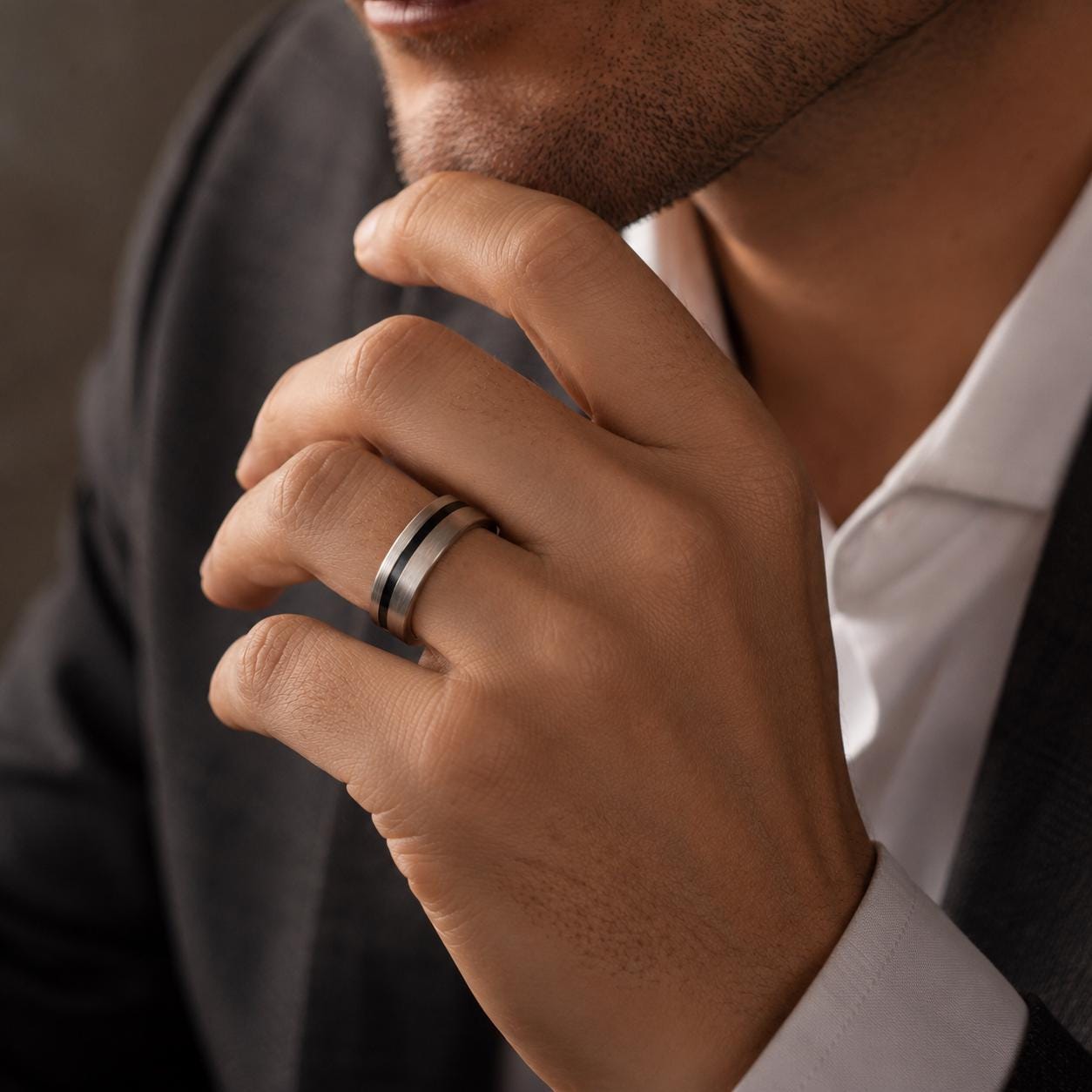 A close-up of a man's hand wearing a ring, with his hand resting on his chin.
