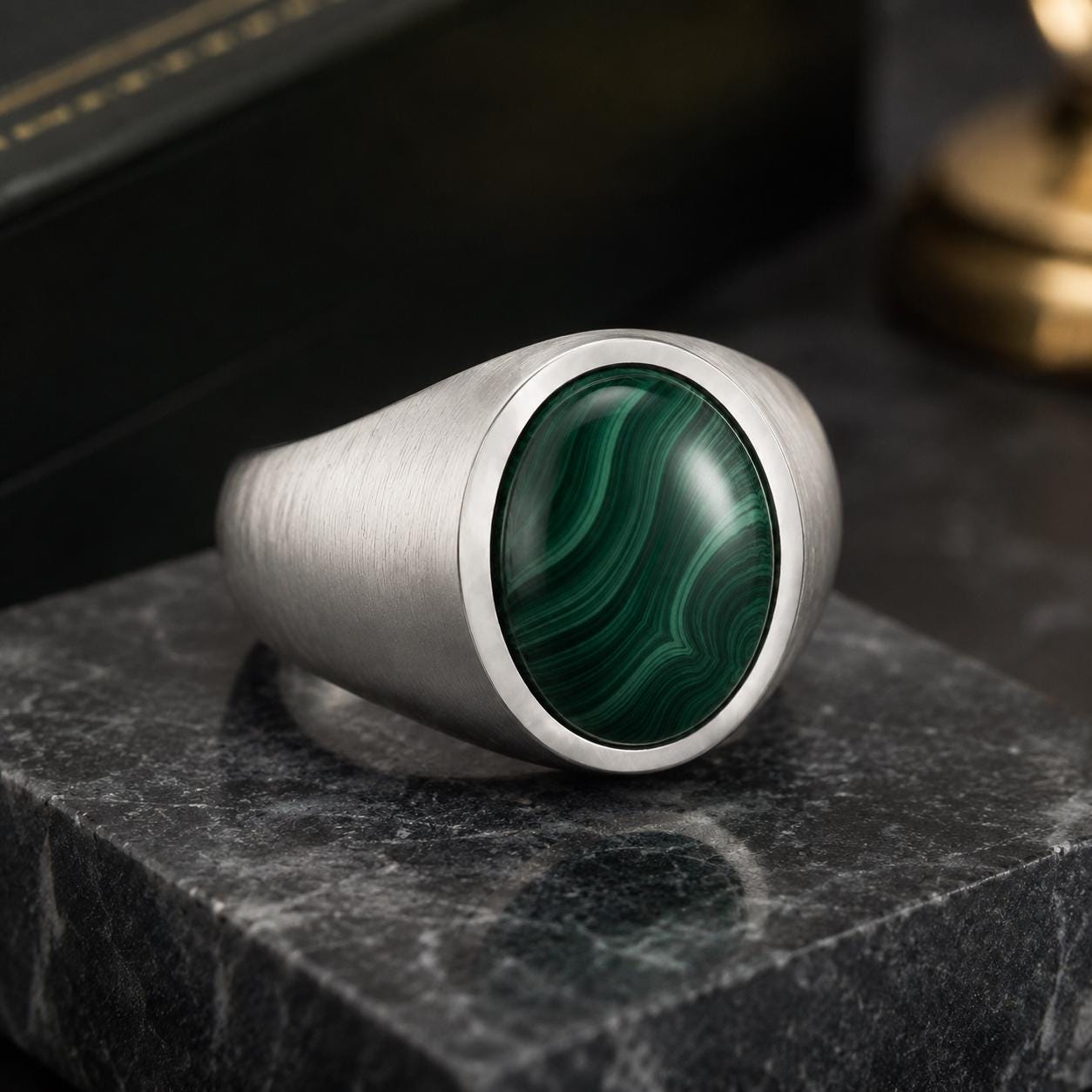 A silver ring with a large, round green malachite stone is displayed on a black marble surface.
