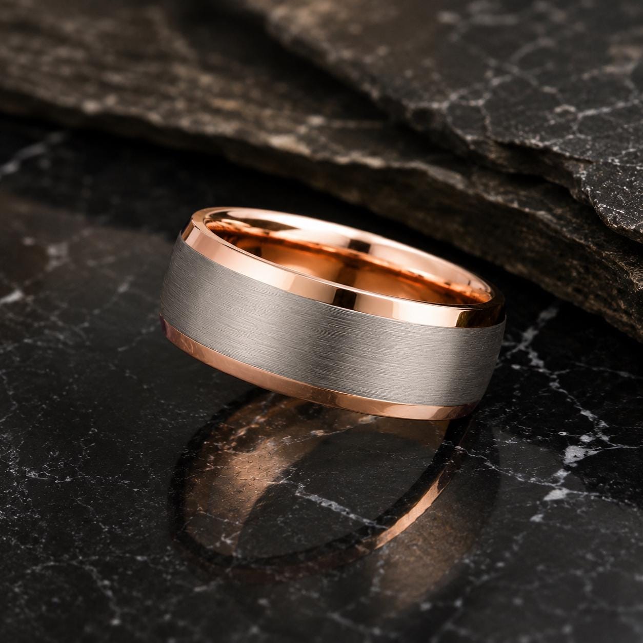 A silver ring with a copper-colored band is resting on a dark, textured surface, such as a marble table.