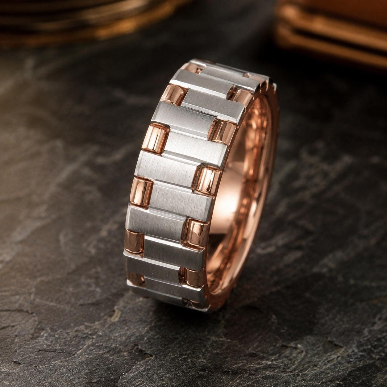 A silver and copper-toned ring with a metallic band is displayed on a dark surface.