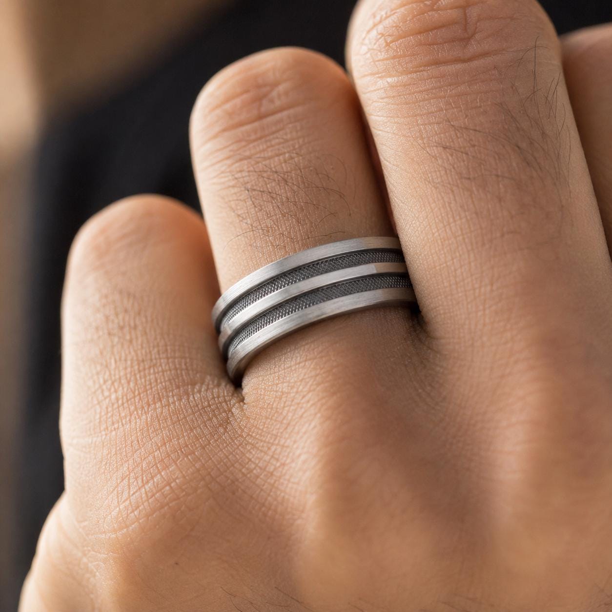 A close-up view of a person's hand wearing a silver ring with a textured band.