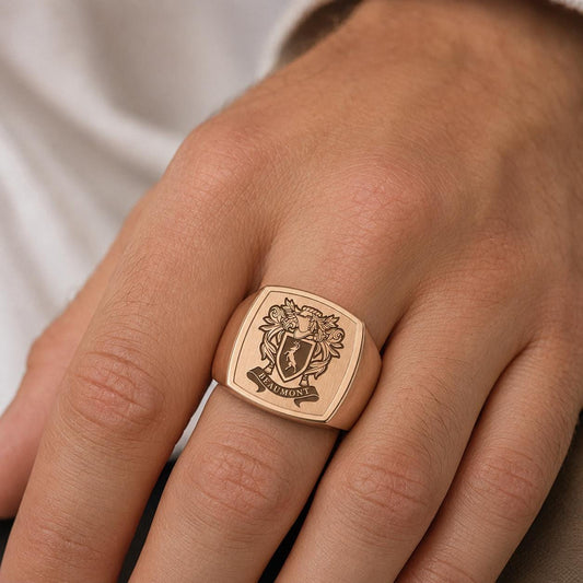 A close-up of a person's hand wearing a gold ring with a crest design on it.