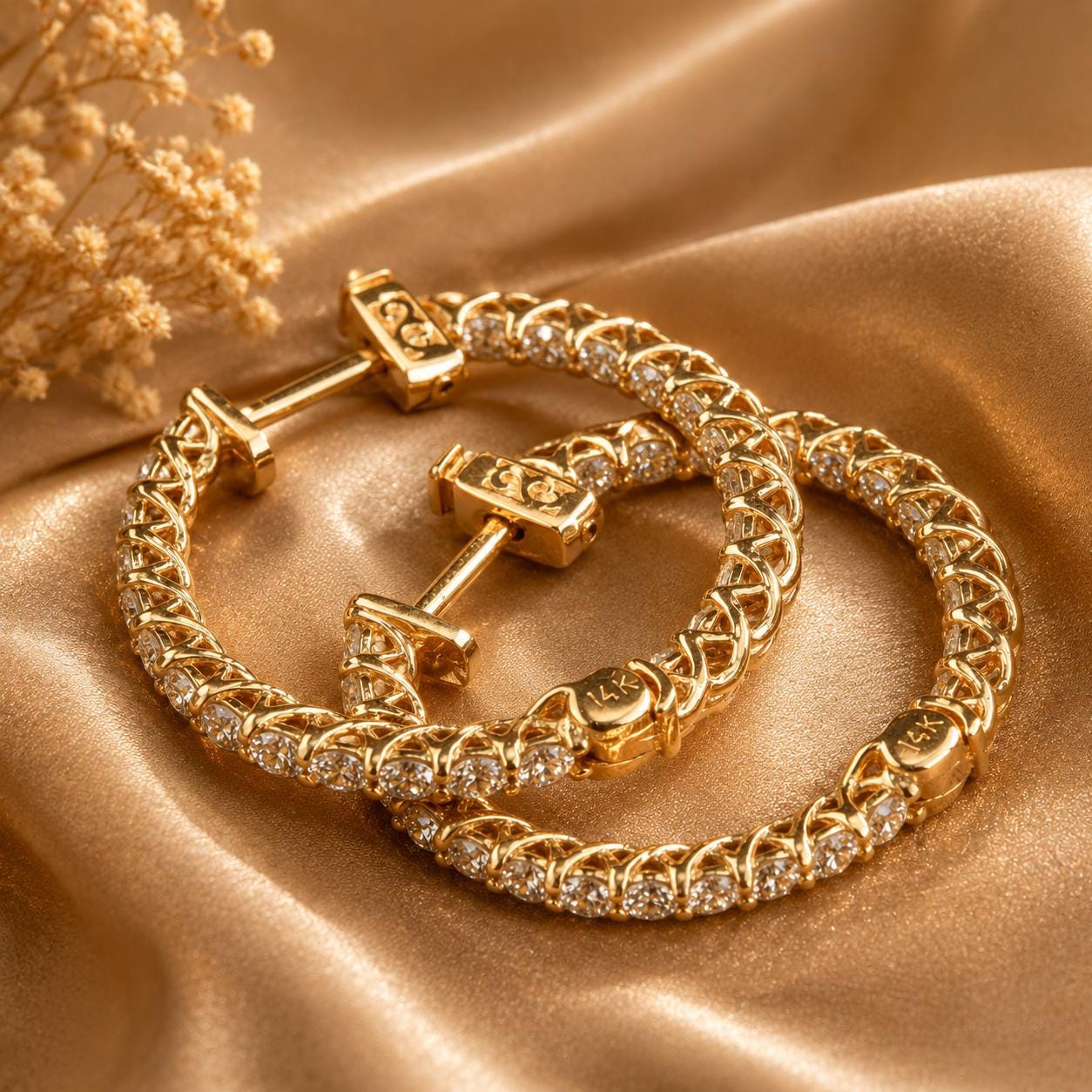 A pair of gold-colored earrings with small diamonds set in the center, resting on a golden fabric background.