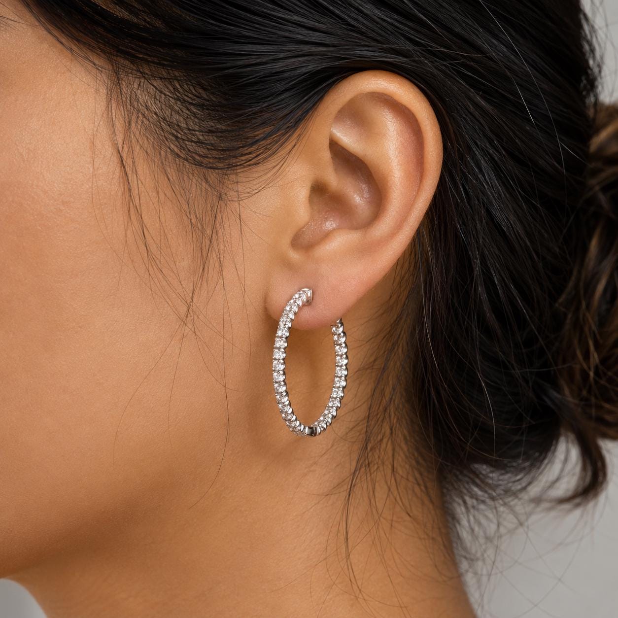 A close-up of a woman's ear wearing a pair of diamond-encrusted hoop earrings.