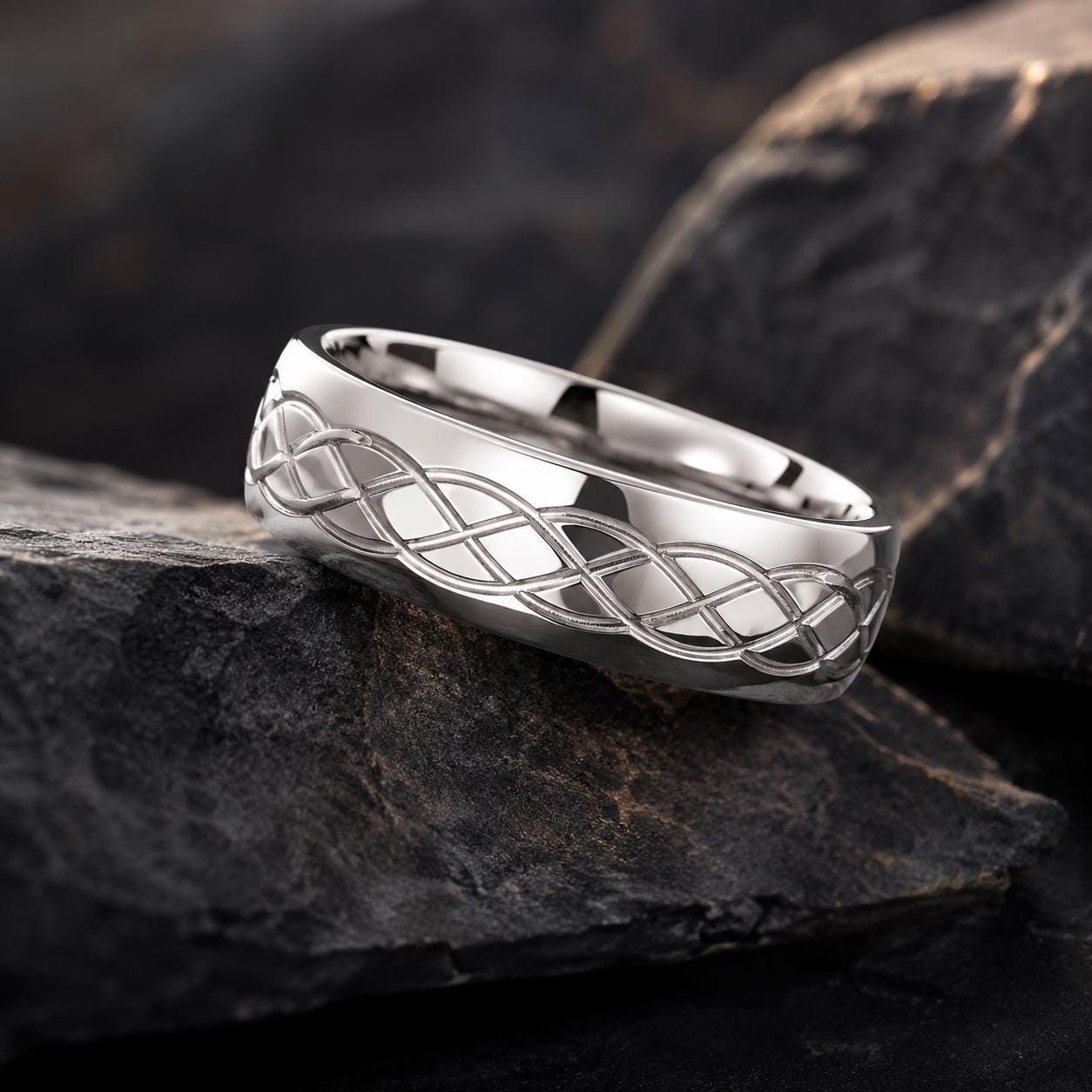 A silver ring with a Celtic knot design is resting on a dark, rocky surface.