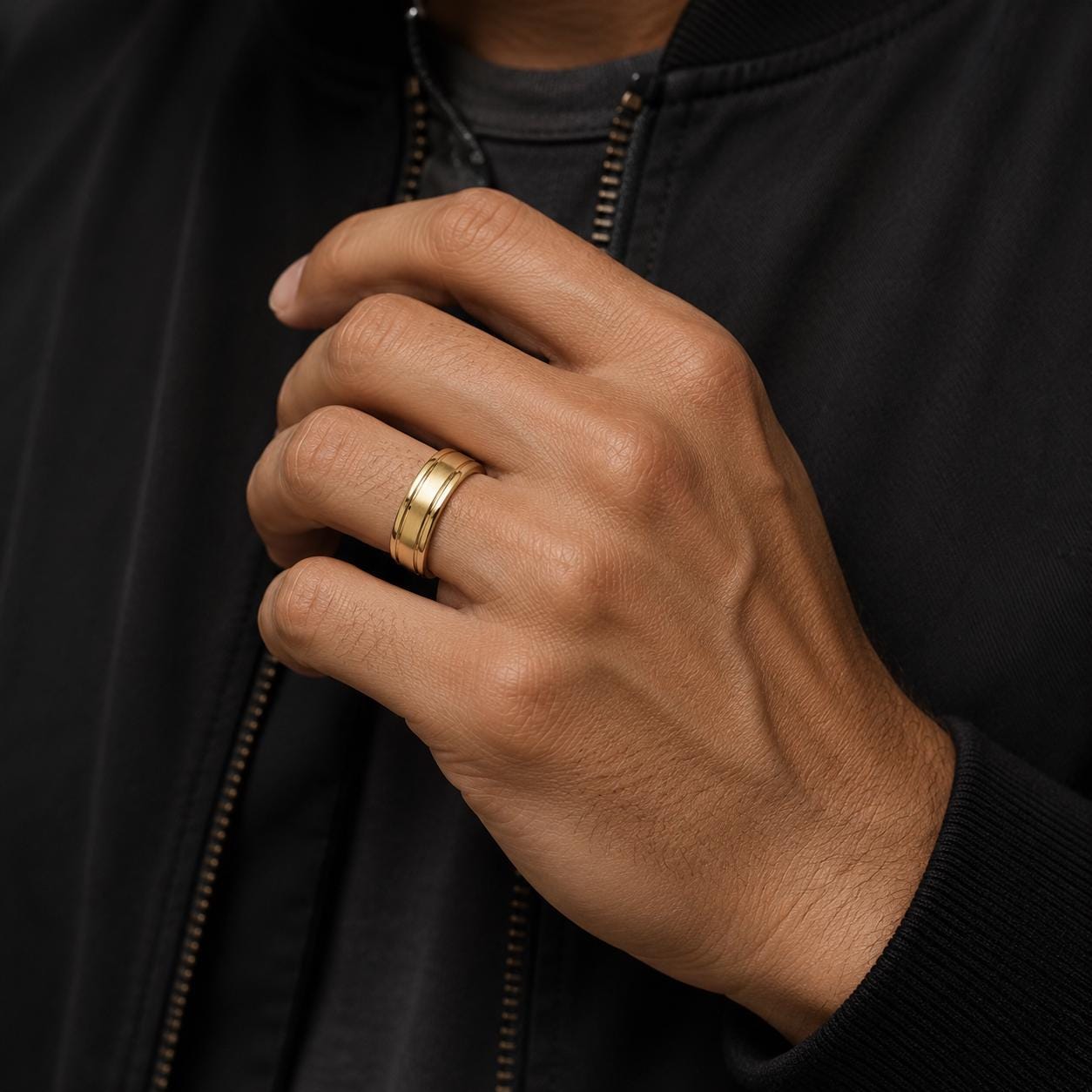 A close-up of a person's hand wearing a gold ring, with a black jacket visible in the background.