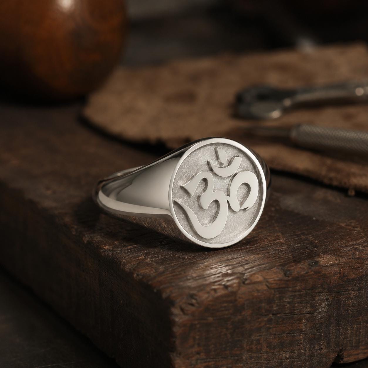 A silver ring with the Om symbol engraved on it, resting on a wooden surface.