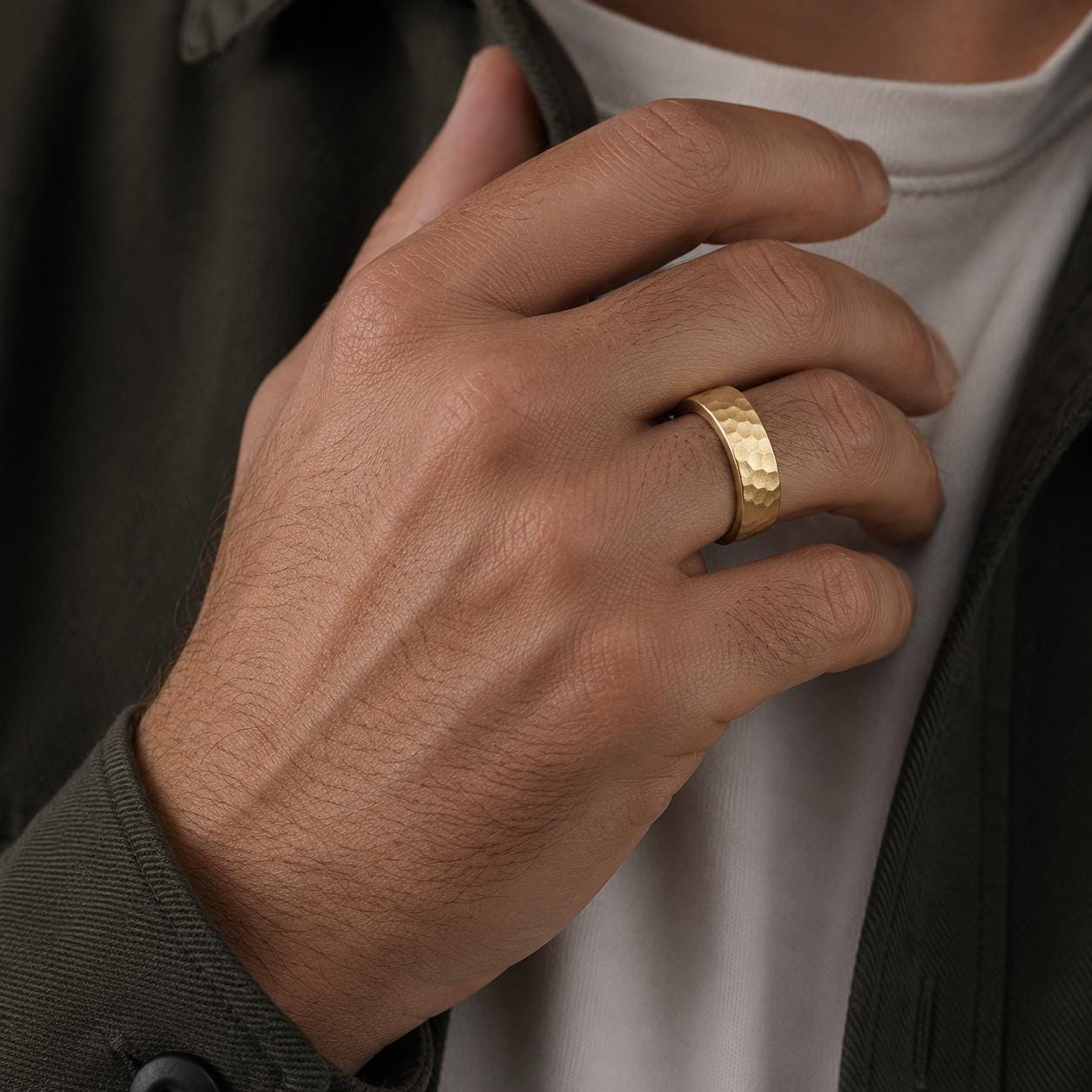 A close-up of a person's hand wearing a gold ring, with a dark jacket visible in the background.