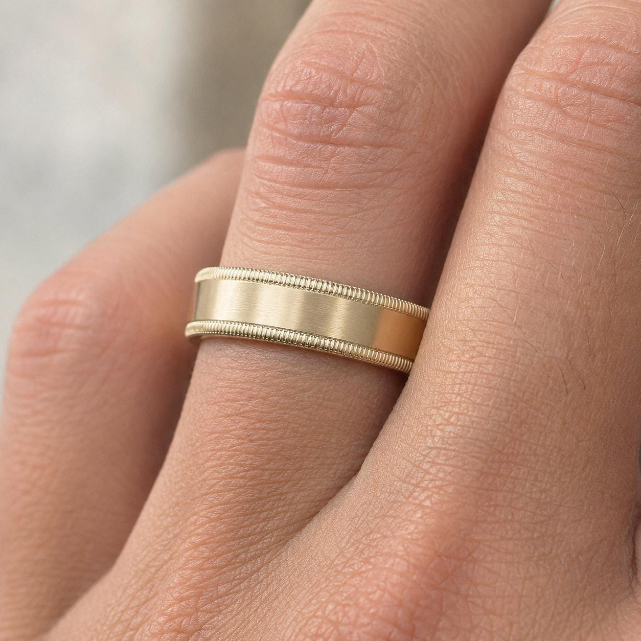 A close-up of a gold wedding band on a person's finger.