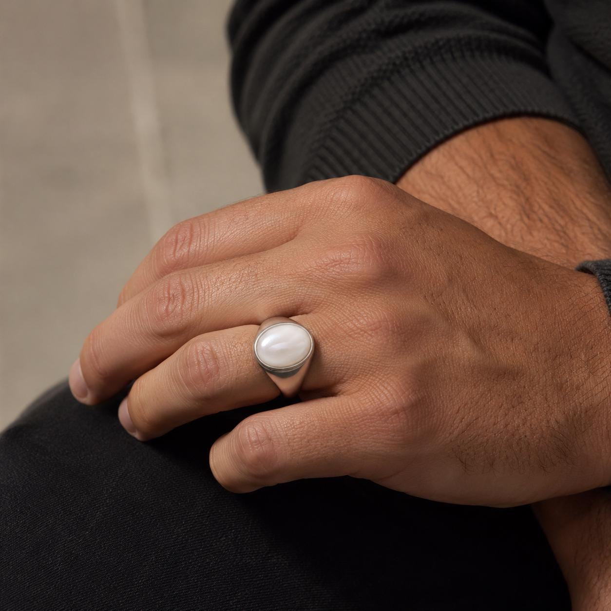 A close-up of a person's hand wearing a silver ring with a white stone.