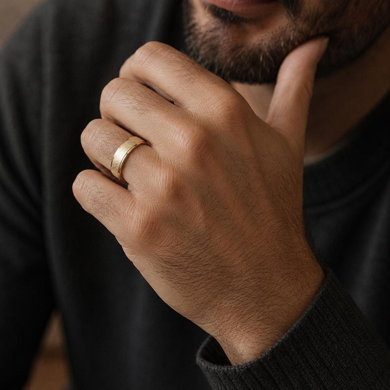 A close-up of a hand wearing a gold ring, with a thoughtful expression on the person's face.