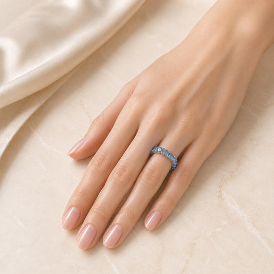 A close-up of a hand wearing a ring with blue stones, resting on a beige surface.