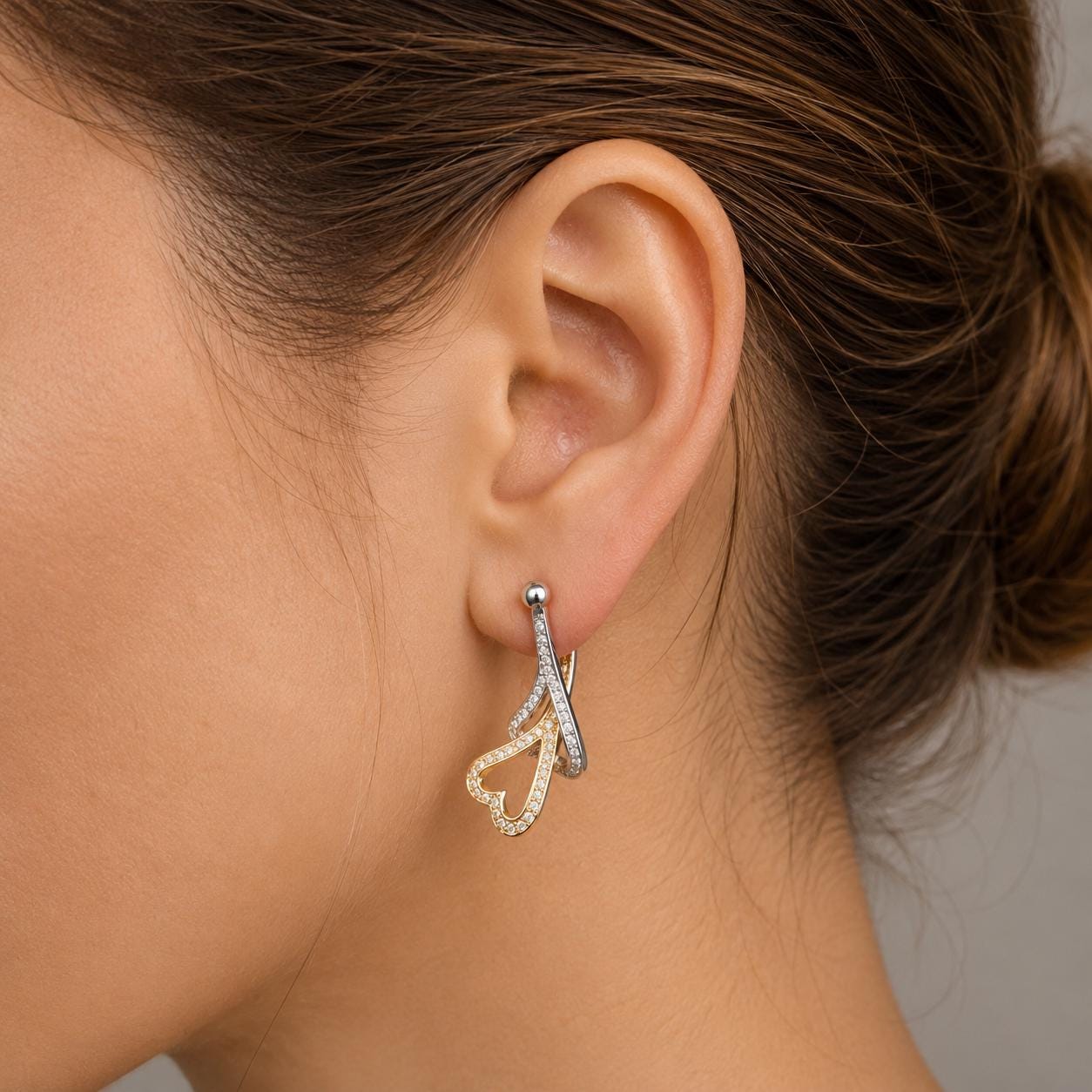 A close-up view of a woman's ear adorned with a pair of earrings featuring a heart-shaped design and sparkling gemstones.