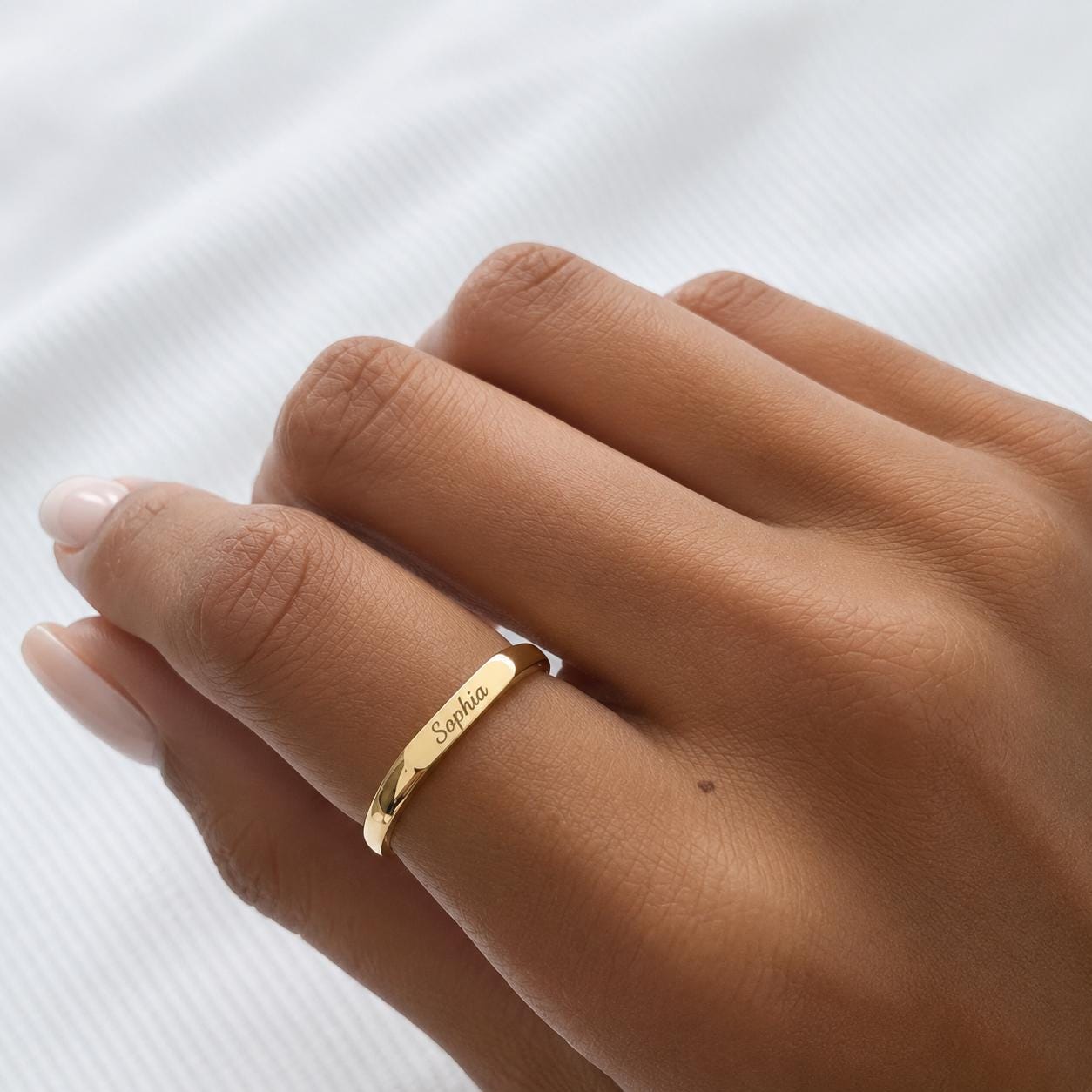 A close-up of a person's hand wearing a gold ring with the name "Sophia" engraved on it.