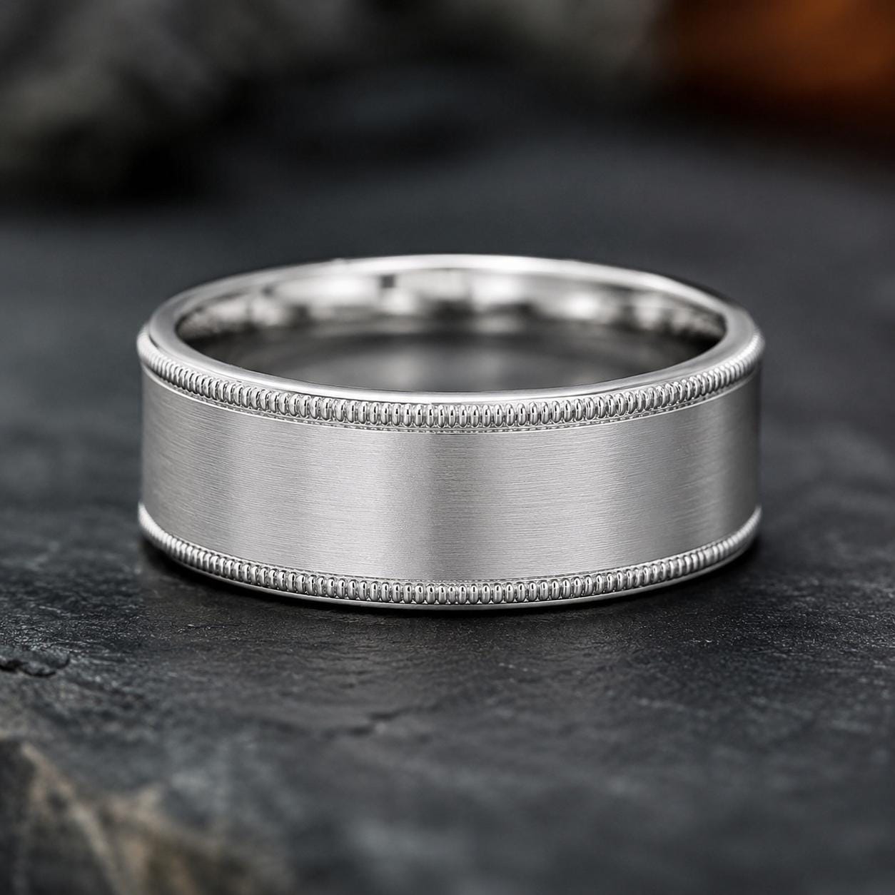 A silver-colored ring with a textured band sits on a dark surface.