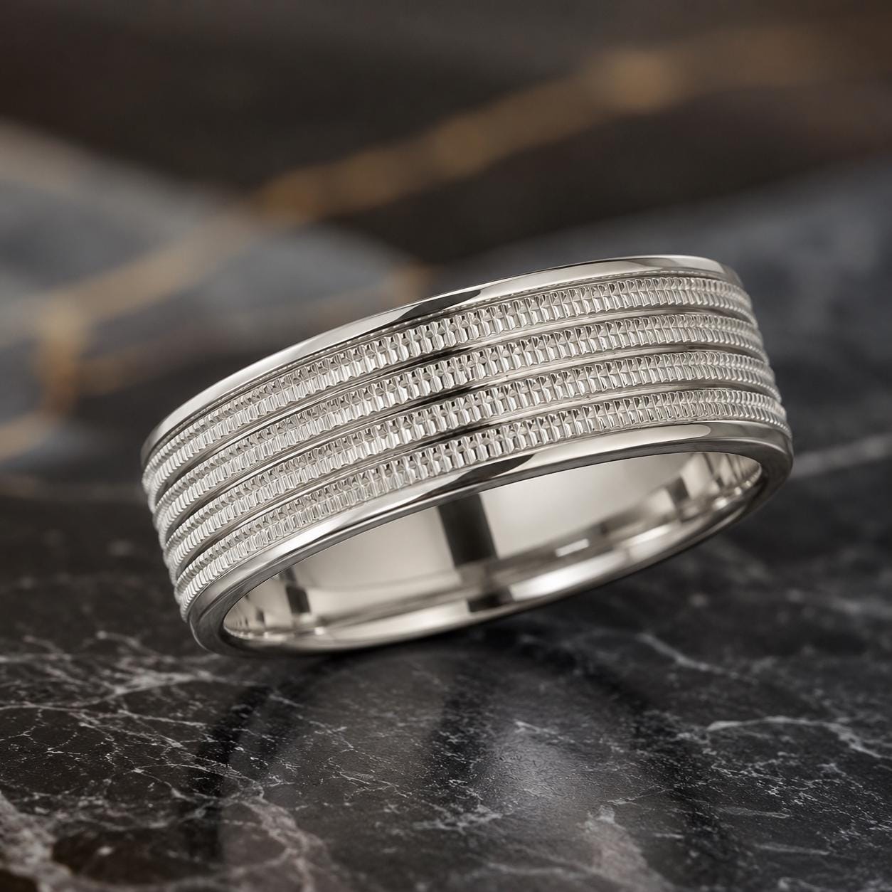 A silver ring with a textured band is displayed on a marble surface.