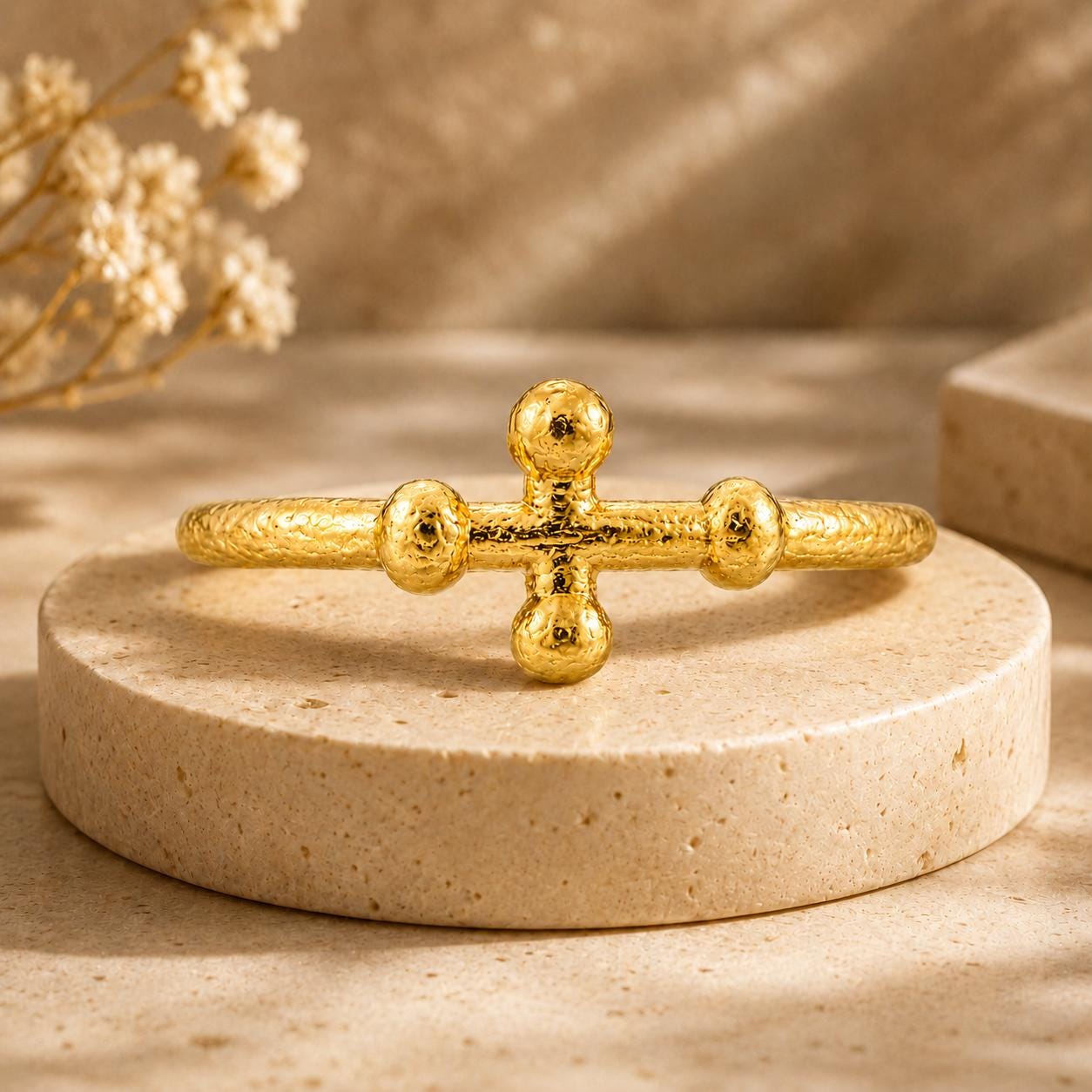 A gold bracelet with a cross-shaped design sits on a round stone surface.