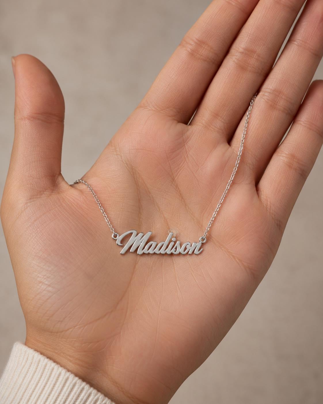 A hand holding a necklace with the name "Madison" engraved on it.